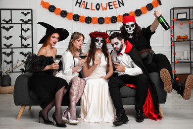Group of people in scary costumes with cocktails celebrating Halloween indoors
