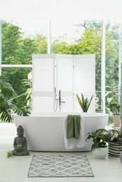 Photo of Stylish bathroom interior with modern tub, window and beautiful houseplants. Home design