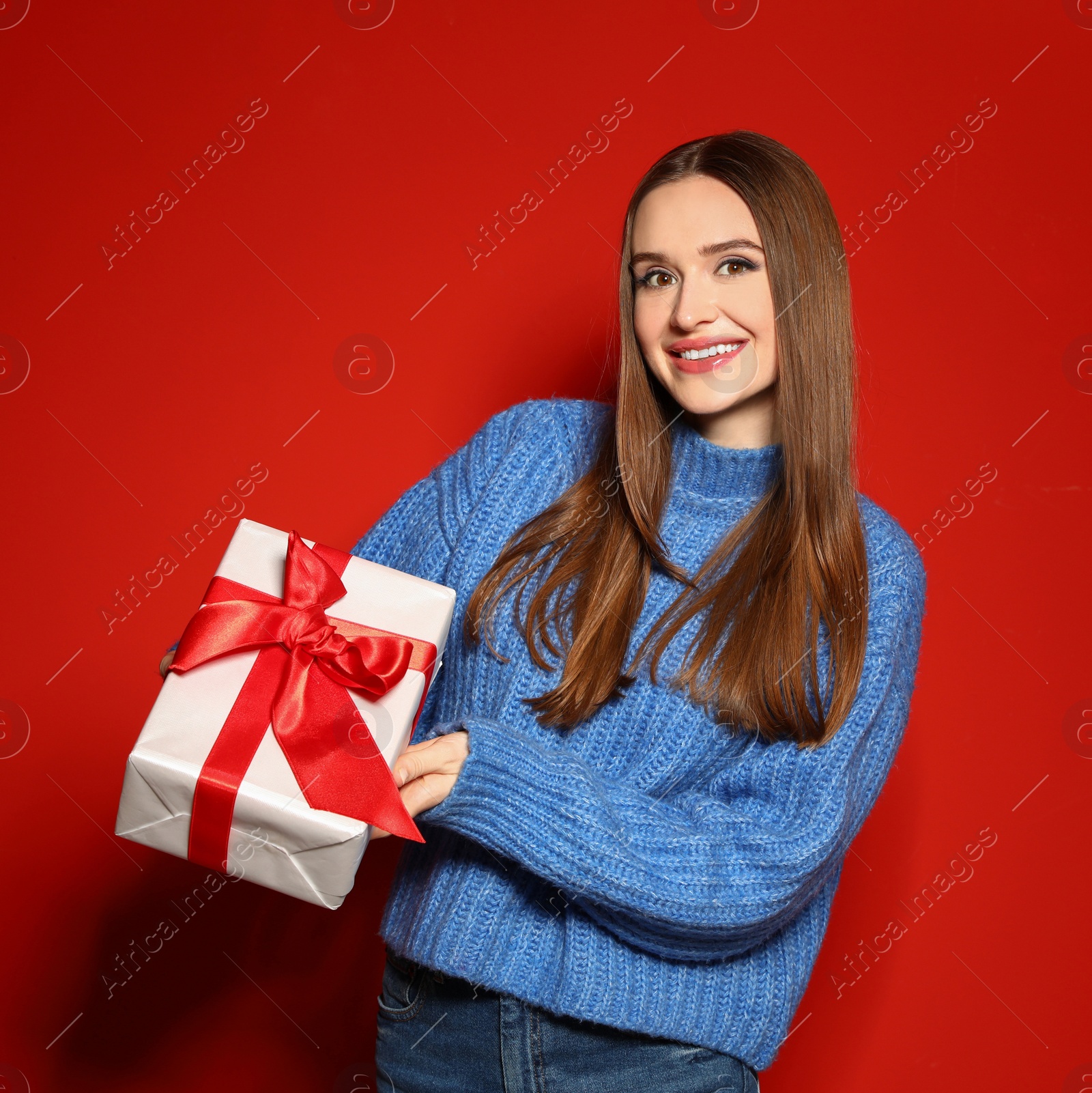 Photo of Young woman in Christmas sweater holding gift box on red background