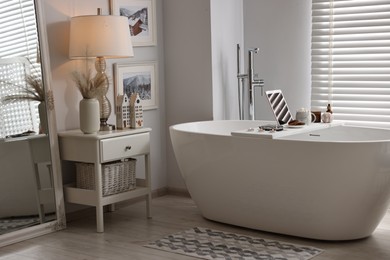 White wooden tray with tablet, spa products and burning candles on bathtub in bathroom