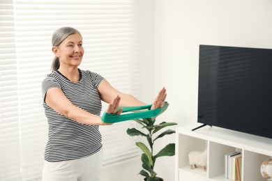 Photo of Senior woman doing exercise with fitness elastic band at home. Space for text