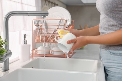 Photo of Woman washing cup at sink in kitchen, closeup