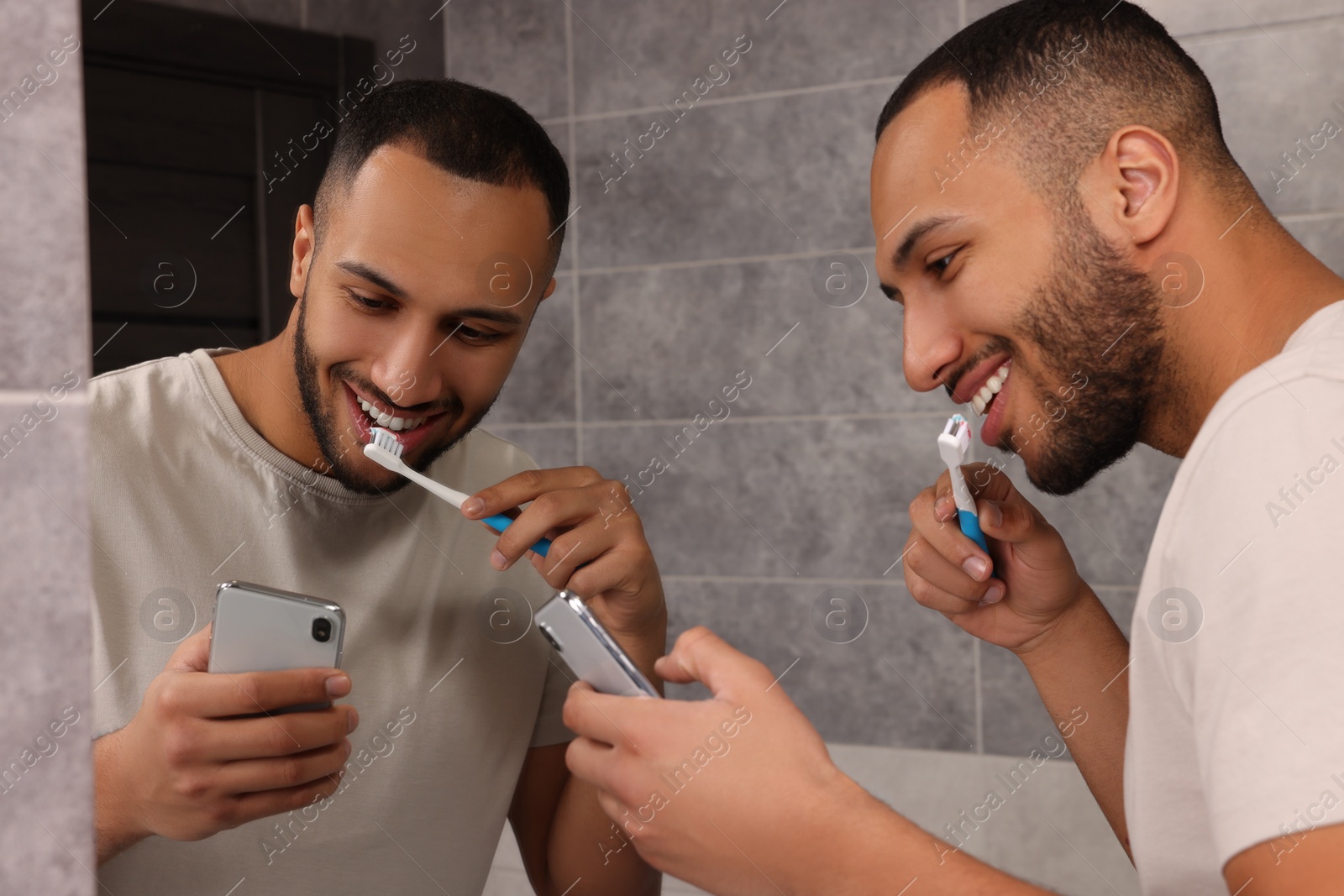 Photo of Happy man using smartphone while brushing teeth in bathroom. Internet addiction