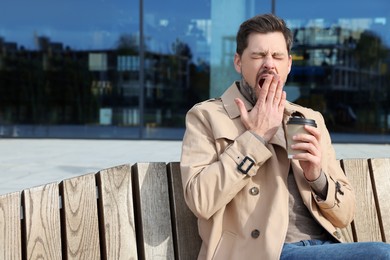 Photo of Sleepy man with cup of coffee yawning outdoors
