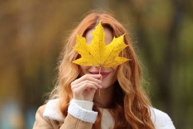 Photo of Woman covering face with autumn leaf outdoors
