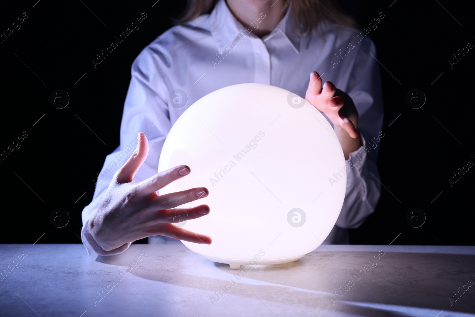 Photo of Businesswoman using glowing crystal ball to predict future at table in darkness, closeup. Fortune telling