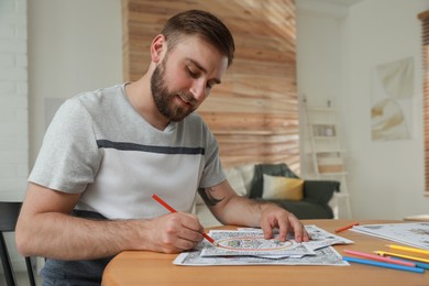 Young man coloring antistress picture at table indoors