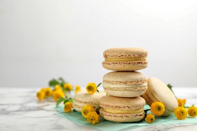Photo of Delicious macarons and flowers on white marble table