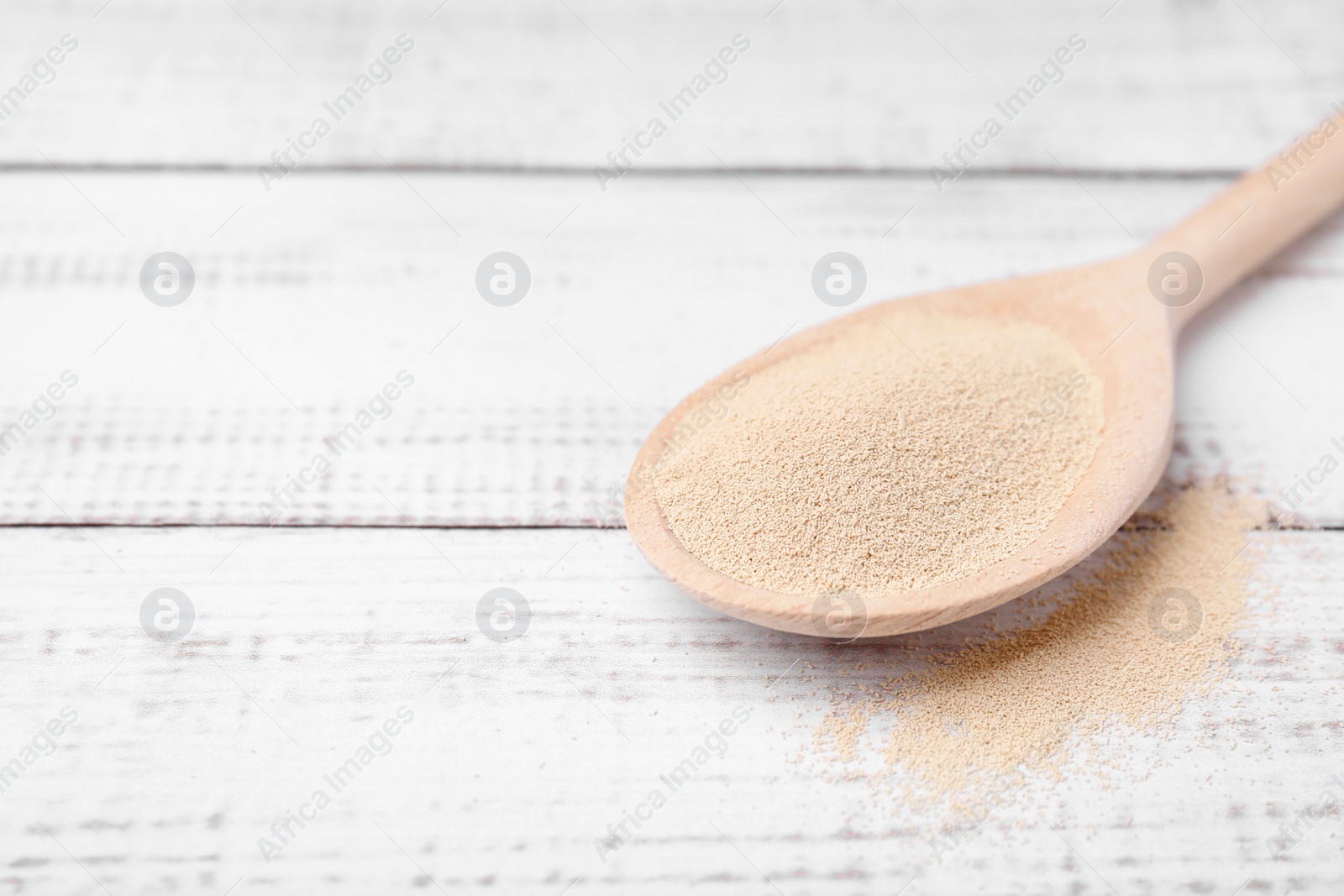 Photo of Spoon with granulated yeast on white wooden table, closeup. Space for text