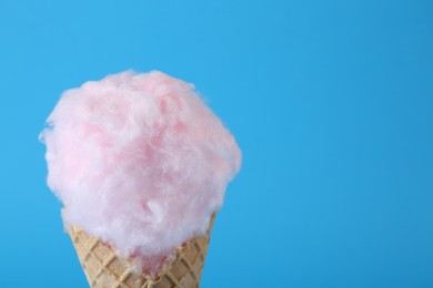 Photo of Sweet cotton candy in waffle cone on light blue background, closeup. Space for text