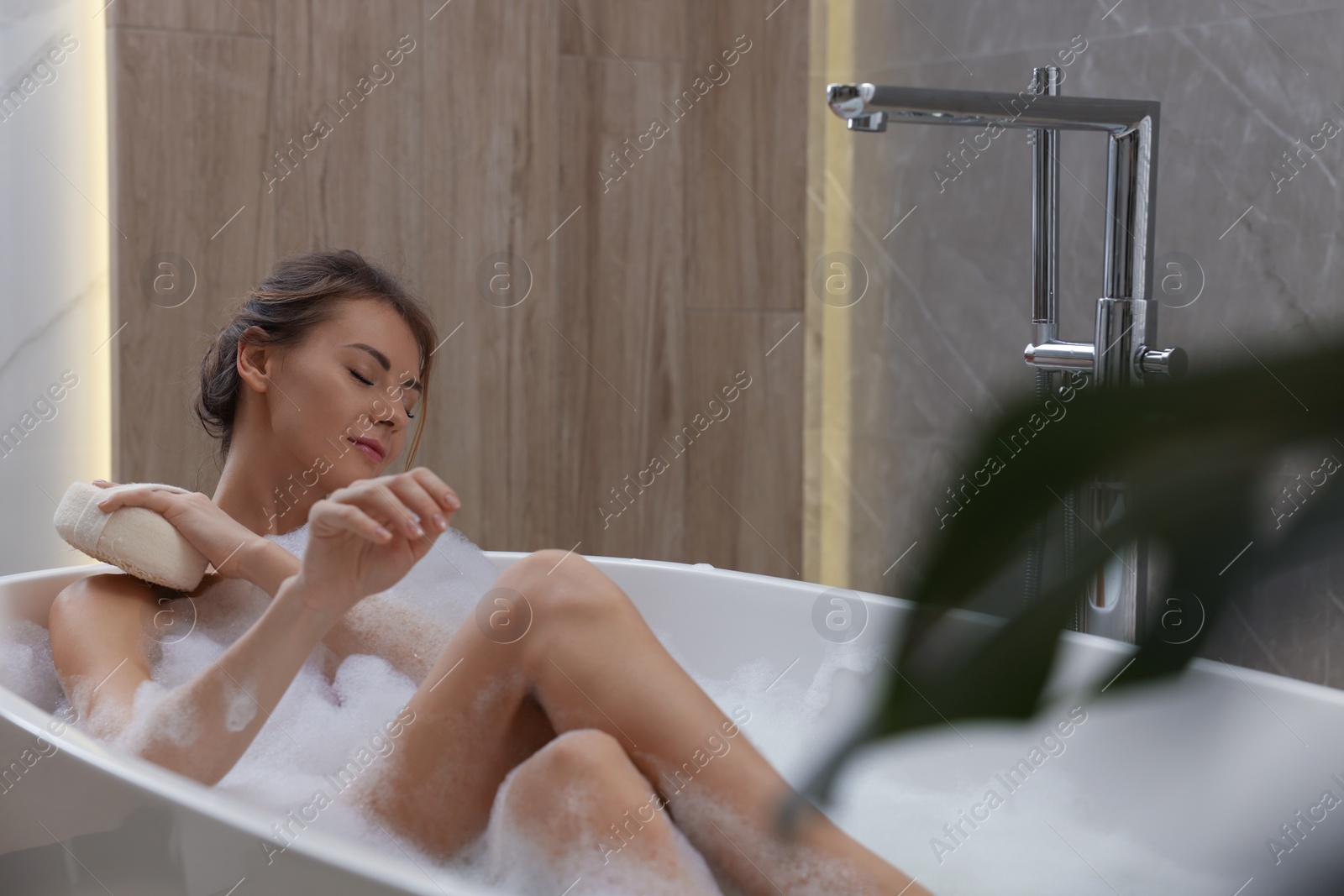 Photo of Beautiful woman with sponge taking bath indoors, space for text