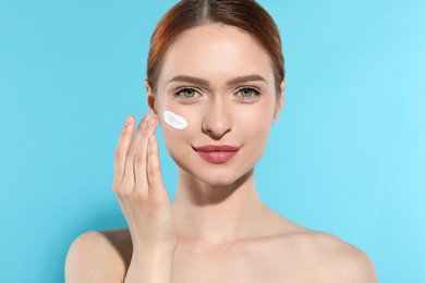 Photo of Beautiful young woman with sun protection cream on her face against light blue background