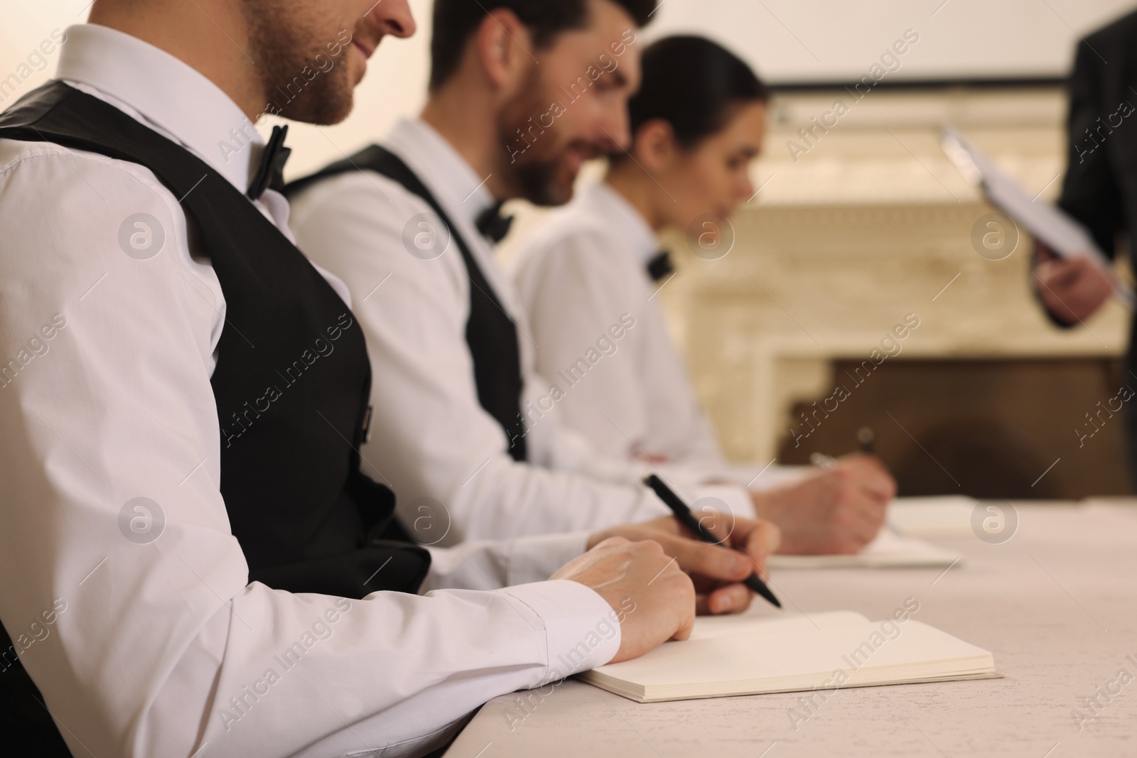 Photo of People writing notes in notebooks at table during lecture, closeup. Professional butler courses