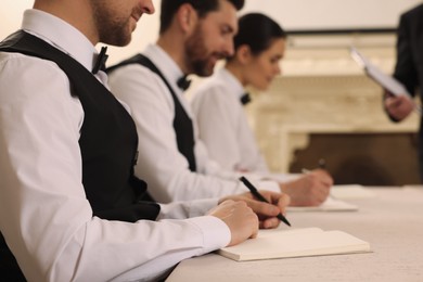 People writing notes in notebooks at table during lecture, closeup. Professional butler courses