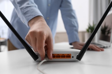 Photo of Woman connecting cable to router at white table indoors, closeup. Wireless internet communication