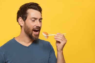 Happy man eating tasty sushi with chopsticks on orange background. Space for text