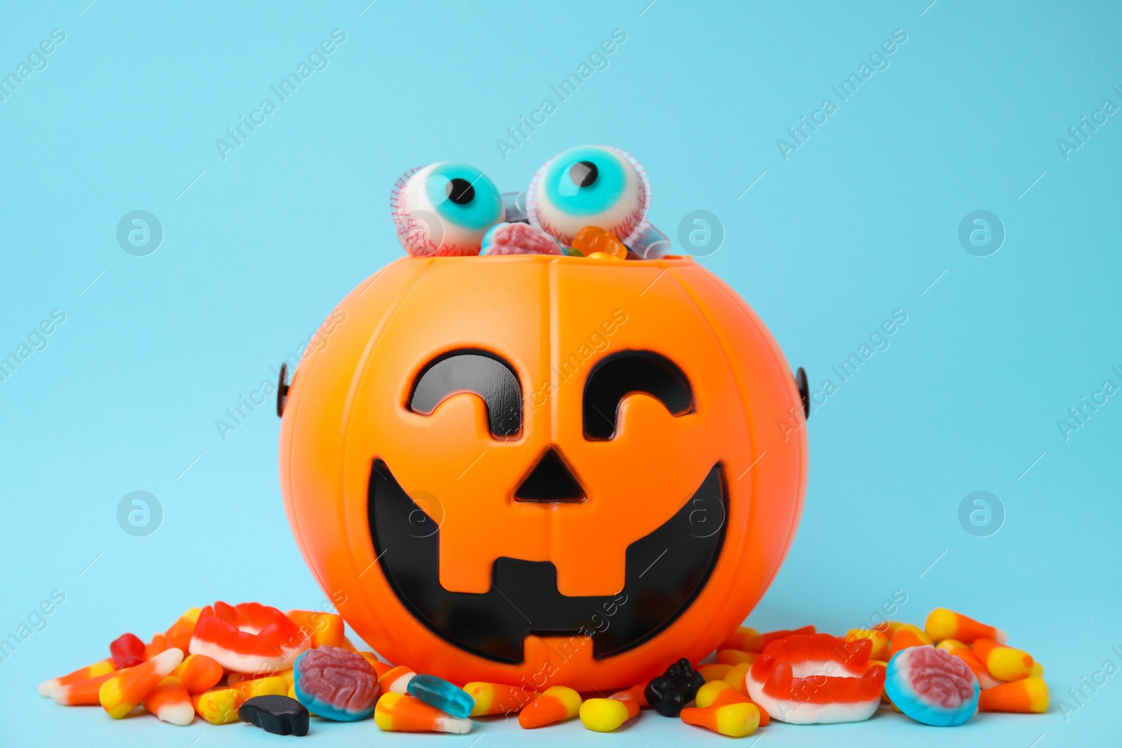Photo of Halloween trick or treat bucket with different sweets on light blue