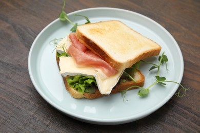 Tasty sandwich with brie cheese and prosciutto on wooden table, closeup