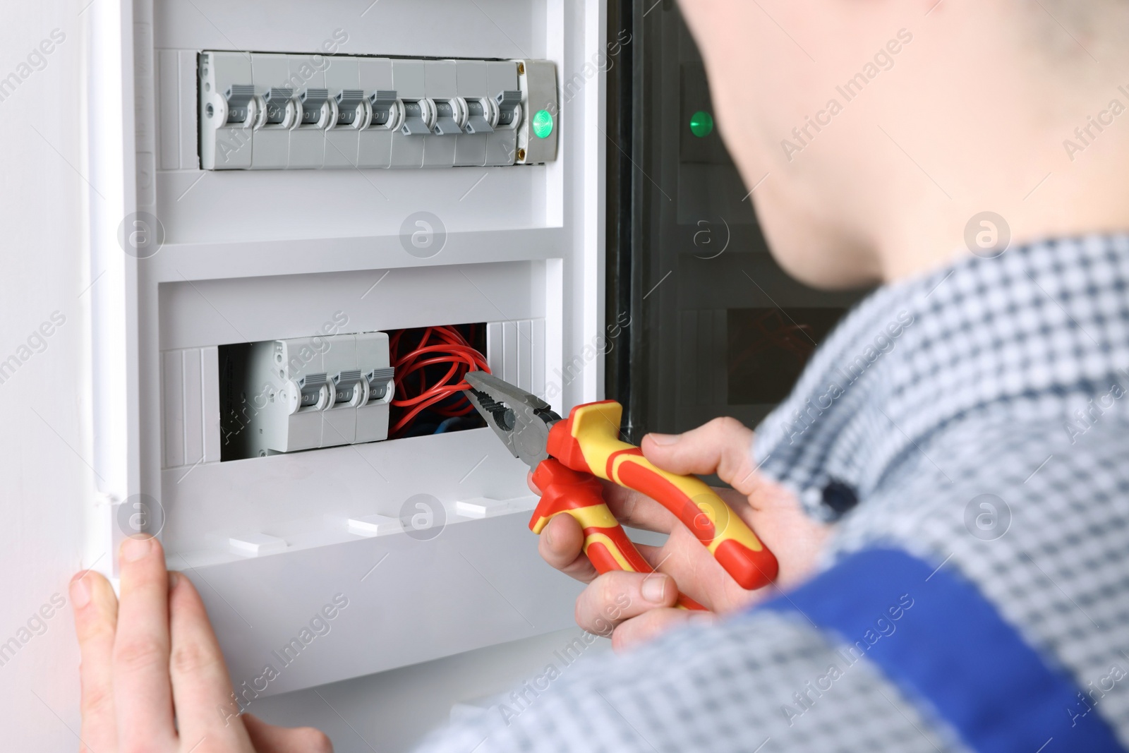 Photo of Professional repairman fixing electric panel with pliers indoors, closeup