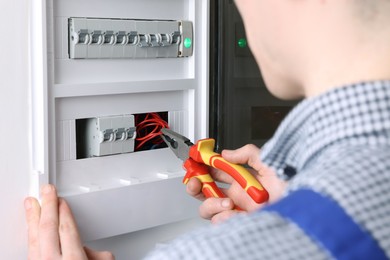 Professional repairman fixing electric panel with pliers indoors, closeup