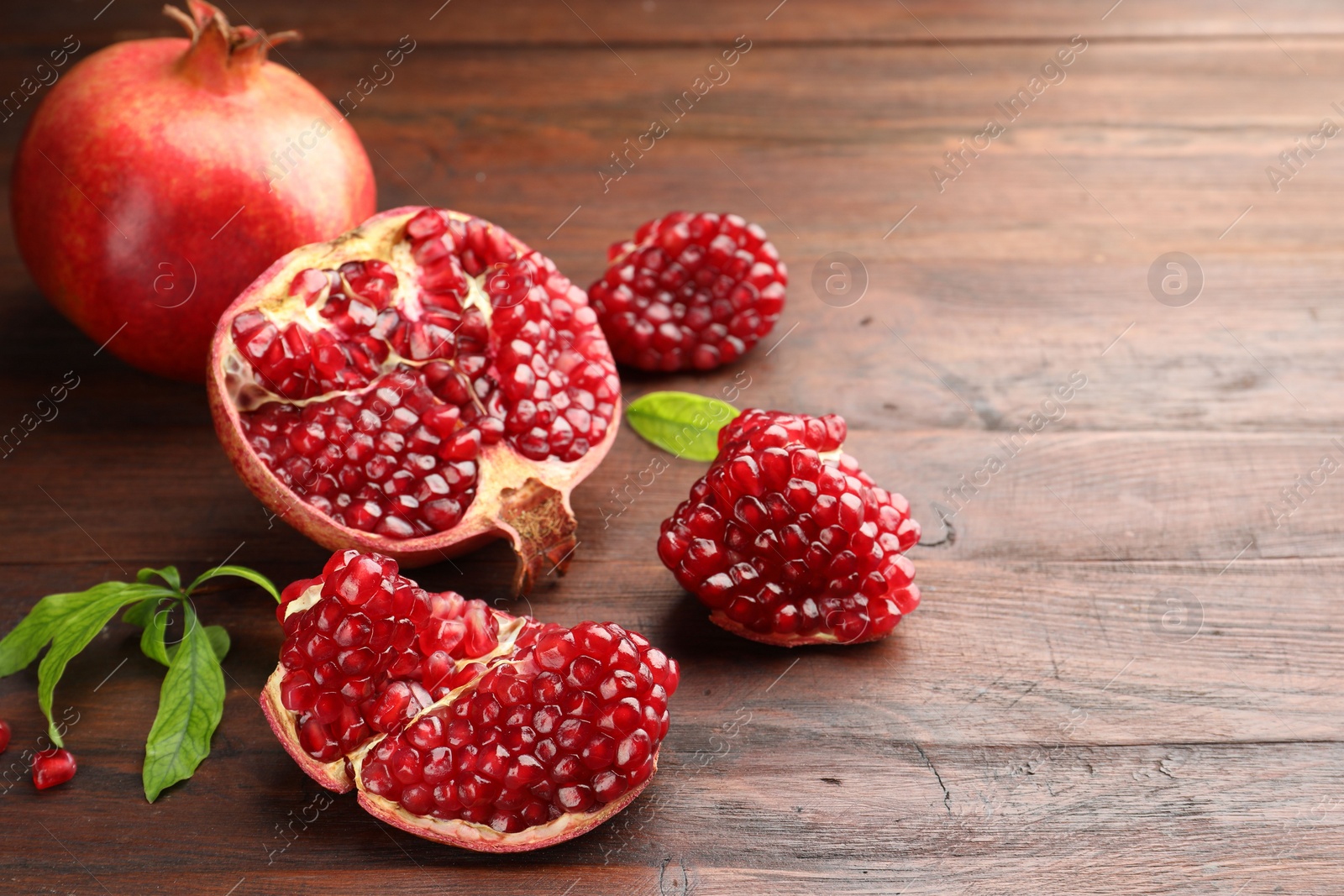 Photo of Fresh pomegranates and green leaves on wooden table, space for text