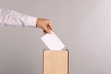 Photo of Man putting his vote into ballot box on light grey background, closeup