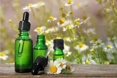 Bottles of essential oil and chamomile flowers on wooden table against blurred background. Space for text