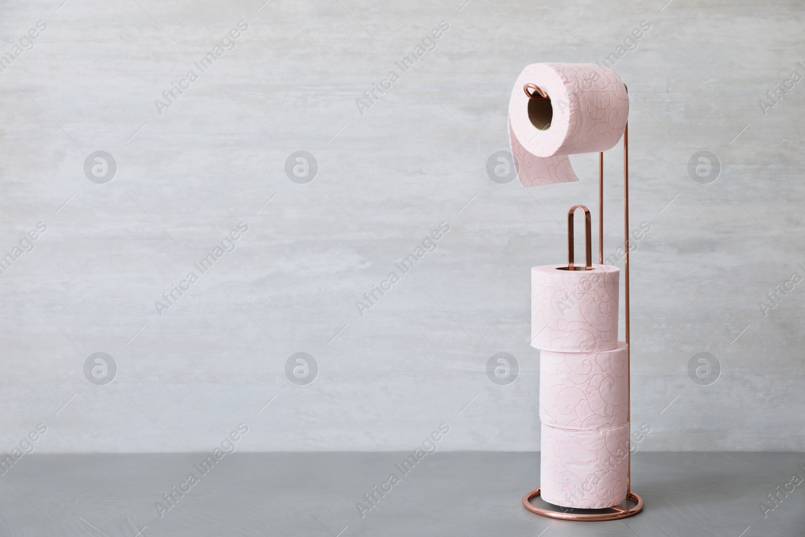 Photo of Holder with toilet paper rolls near gray wall. Space for text