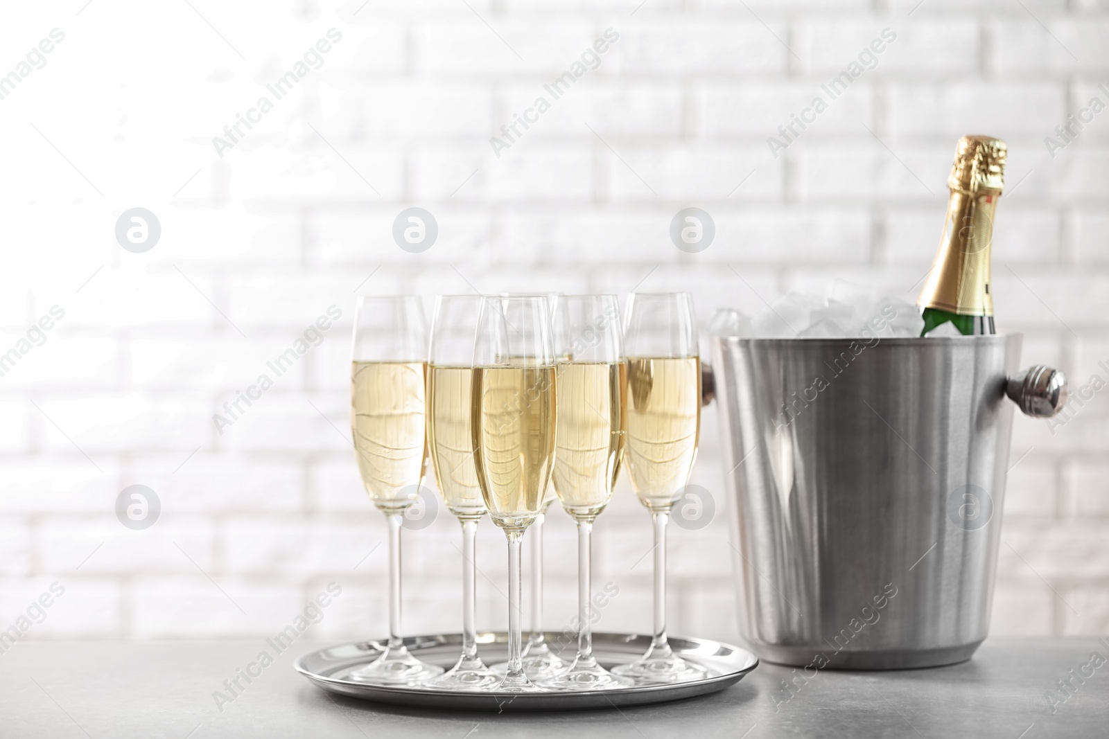 Photo of Glasses with champagne and bottle in bucket on table against brick wall