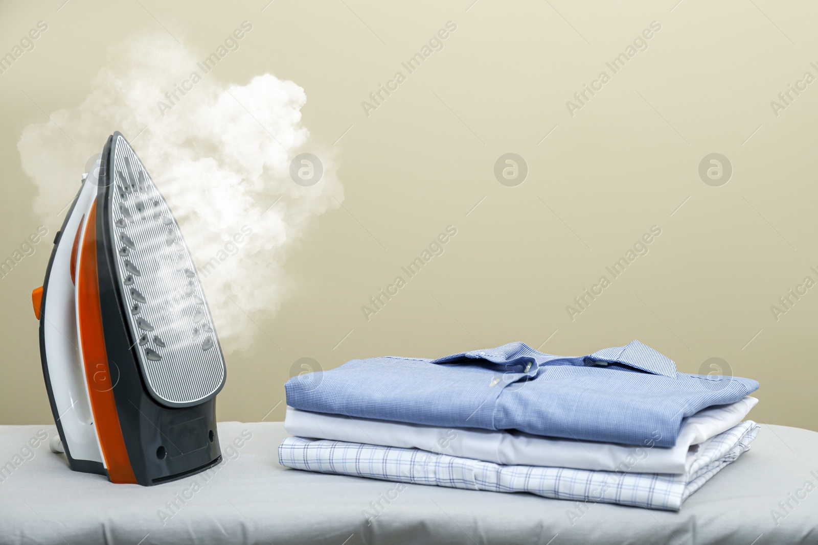 Image of Modern iron with steam and folded clothes on ironing board, space for text