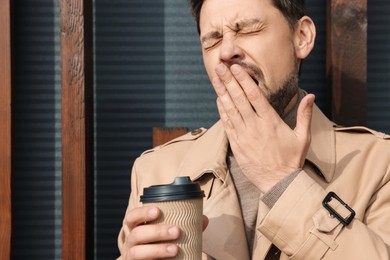Photo of Sleepy man with cup of coffee yawning outdoors, closeup