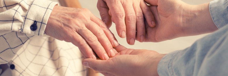 Image of Young and elderly women holding hands indoors, closeup. Banner design