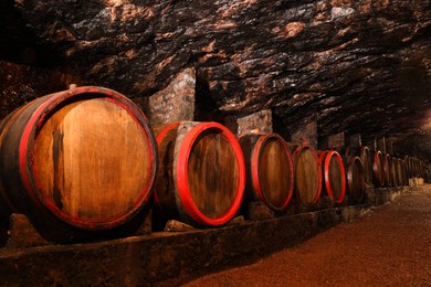 Photo of Many wooden barrels with alcohol drinks in cellar