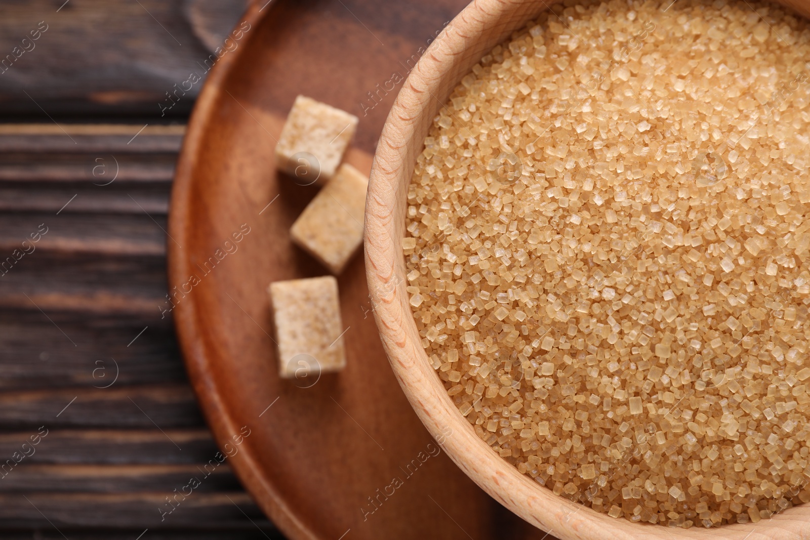 Photo of Brown sugar in bowl and cubes on wooden table, top view