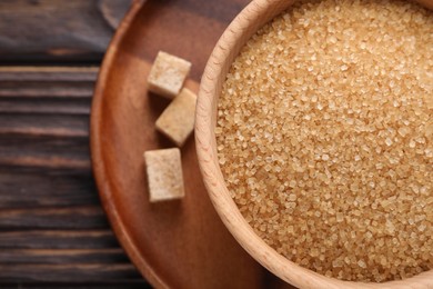 Photo of Brown sugar in bowl and cubes on wooden table, top view