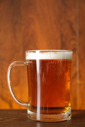 Mug with fresh beer on wooden table against color background