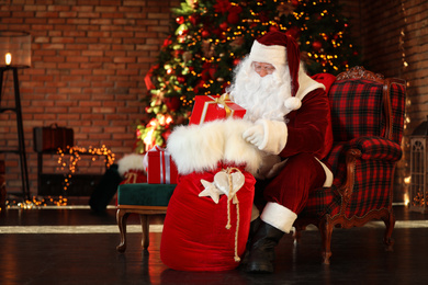 Photo of Santa Claus with gift sack near Christmas tree indoors