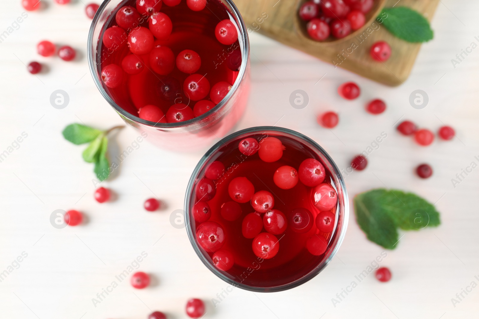 Photo of Tasty cranberry juice in glasses and fresh berries on white wooden table, flat lay