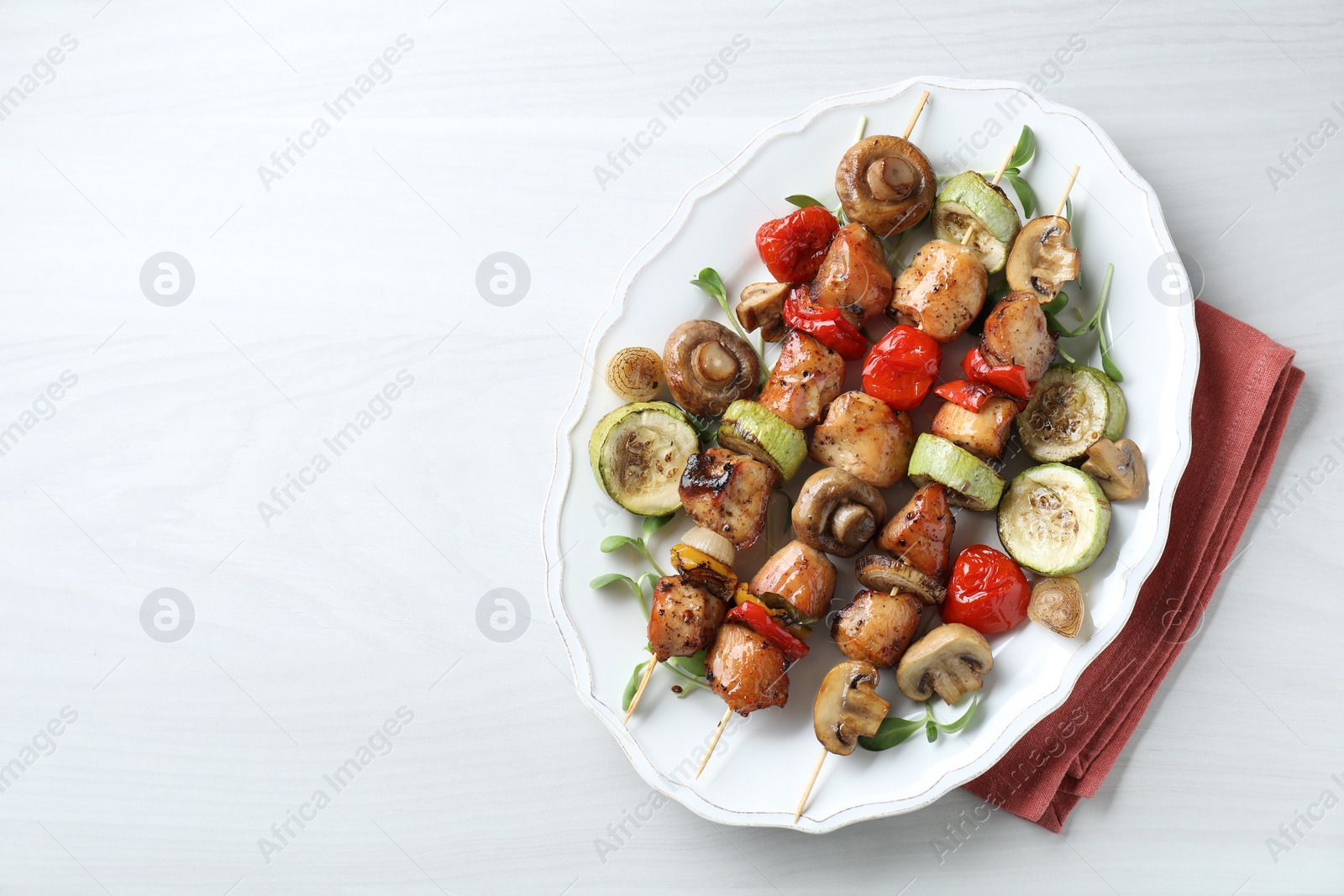 Photo of Delicious shish kebabs with vegetables and microgreens on white table, top view. Space for text