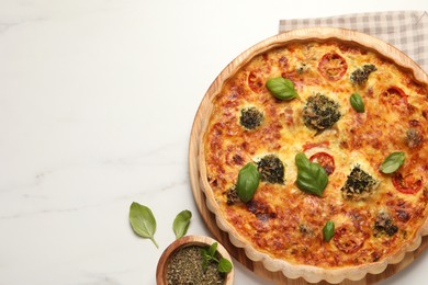 Photo of Delicious homemade vegetable quiche, basil leaves and seasoning on white marble table, flat lay. Space for text