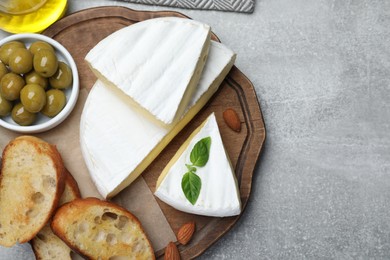 Photo of Tasty brie cheese with olives, basil, bread and almonds on grey table, flat lay. Space for text