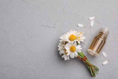 Photo of Flat lay composition with chamomile flowers and cosmetic bottle of essential oil on grey background. Space for text