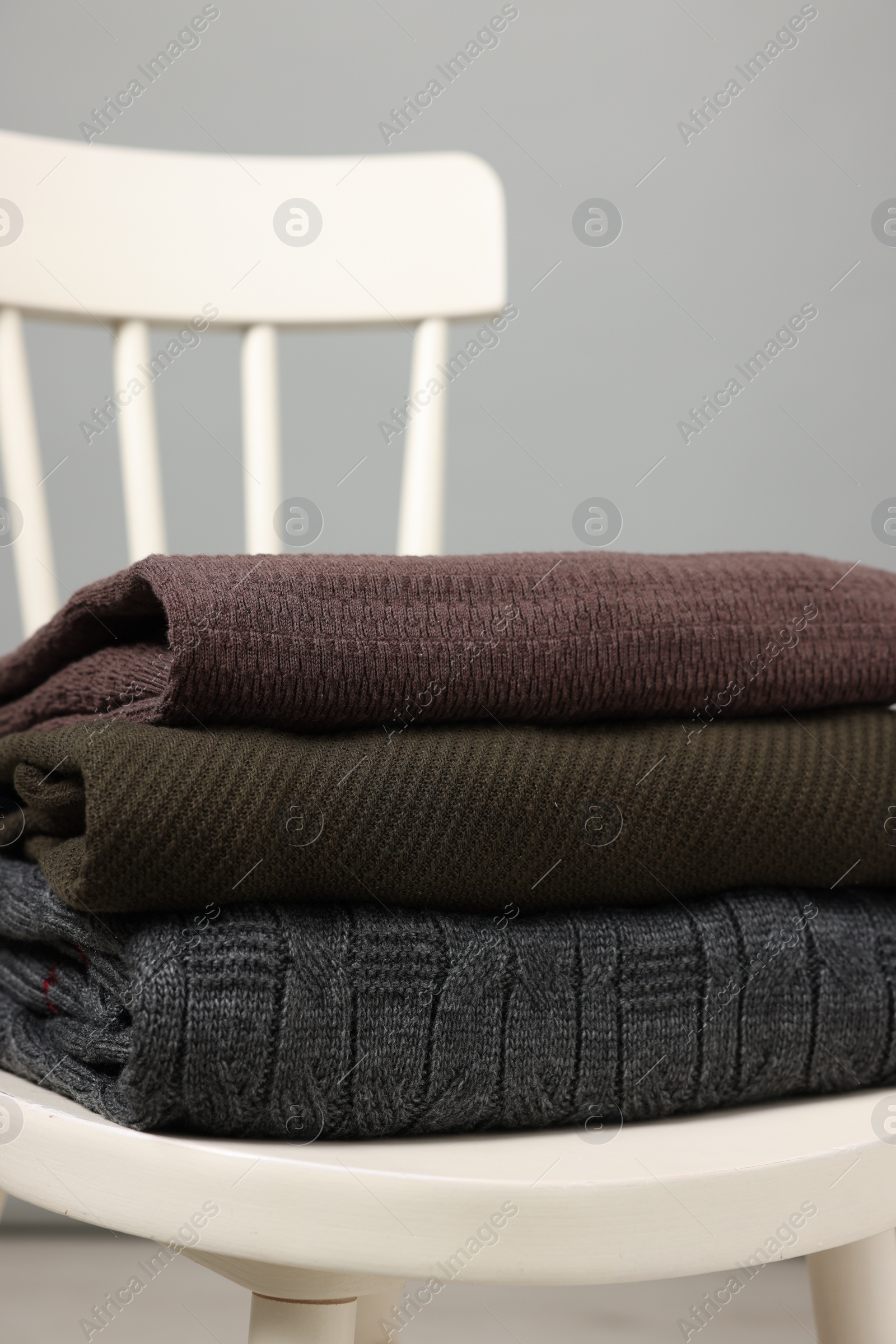 Photo of Stack of different warm sweaters on white chair against grey background, closeup