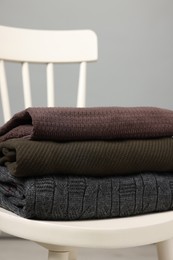 Photo of Stack of different warm sweaters on white chair against grey background, closeup