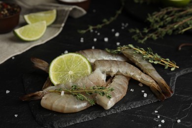 Photo of Fresh raw shrimps with lime and thyme on black table