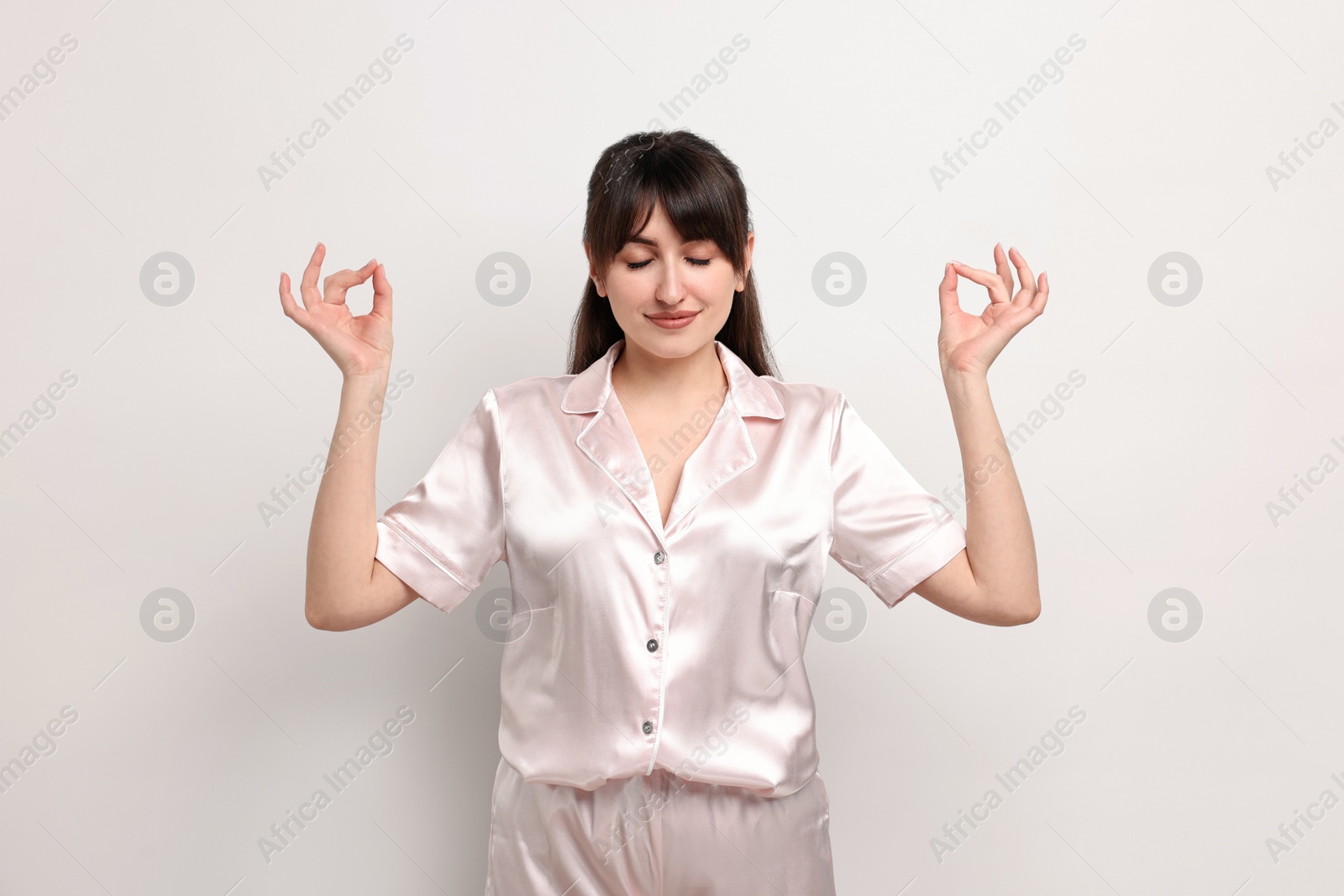 Photo of Woman in pyjama meditating on light grey background