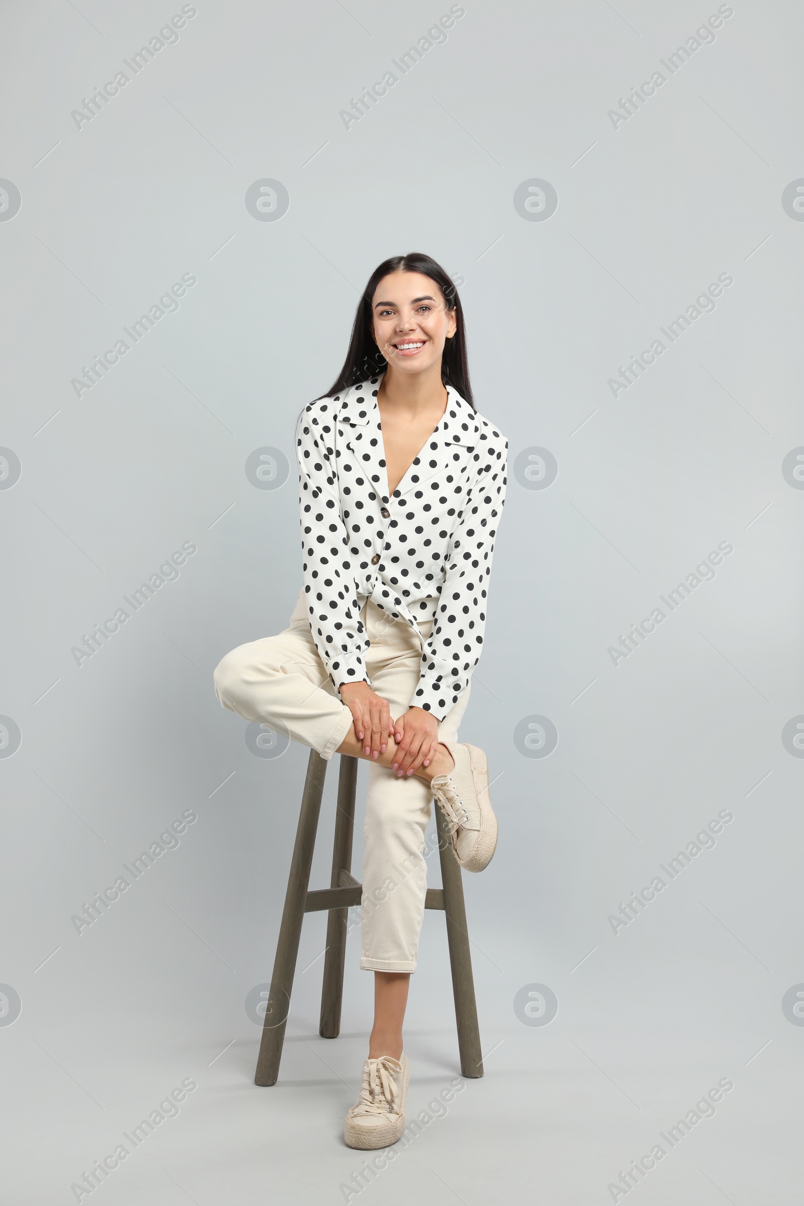 Photo of Beautiful young woman sitting on stool against light grey background