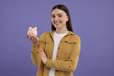 Photo of Happy woman with piggy bank on purple background