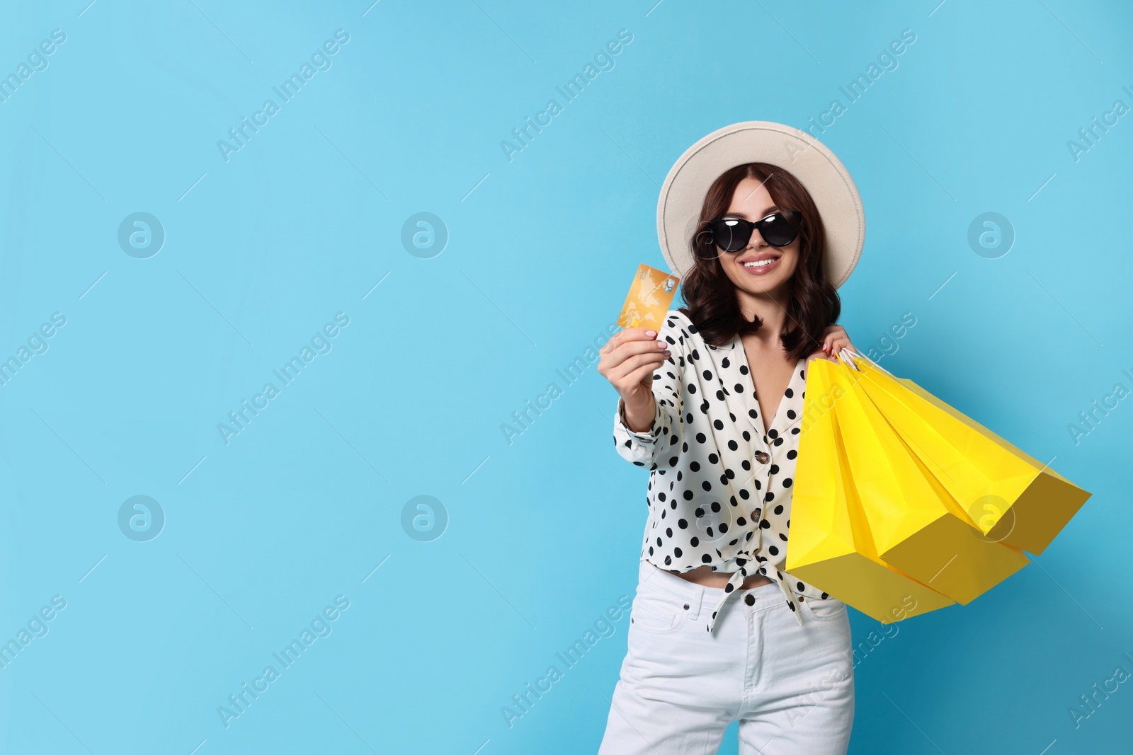 Photo of Beautiful young woman with paper shopping bags and credit card on light blue background. Space for text