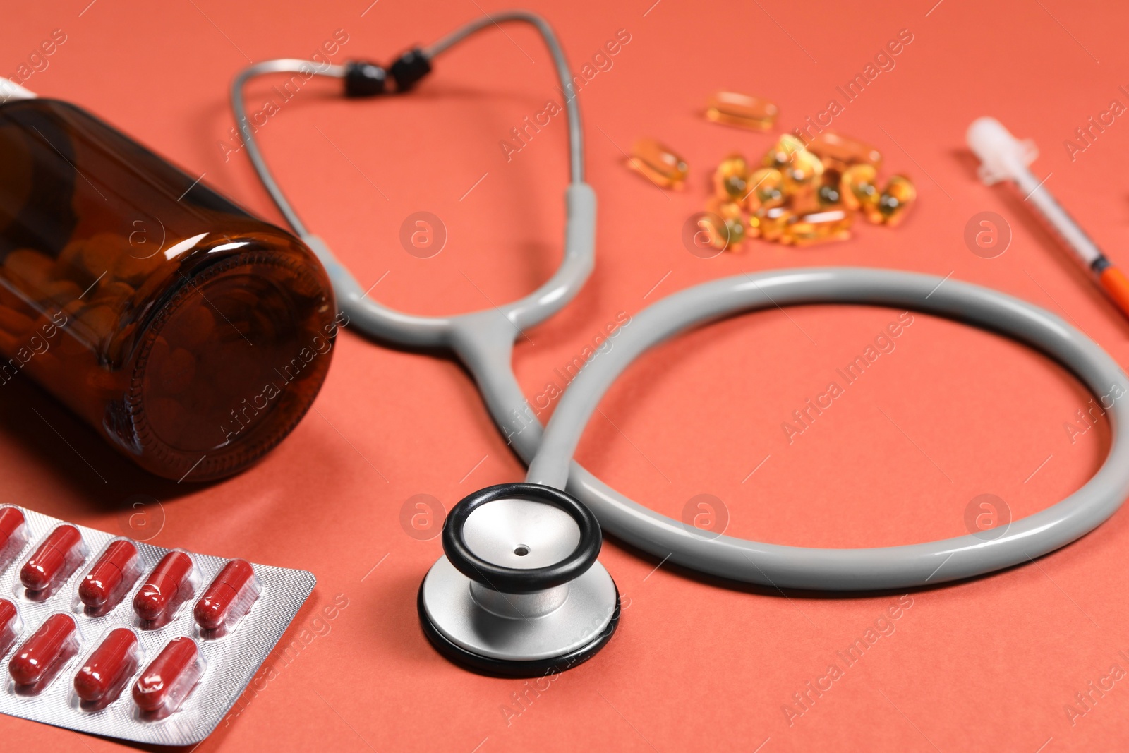 Photo of Stethoscope and pills on crimson background, closeup. Medical tool